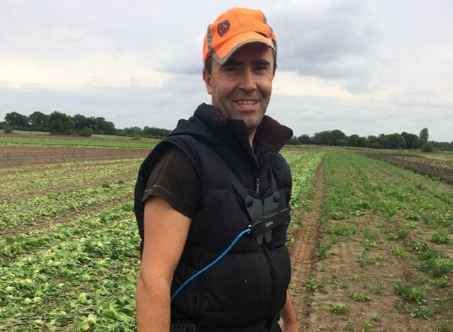 Ein Mann mit Exoskelett steht auf einem landwirtschaftlichen Feld.